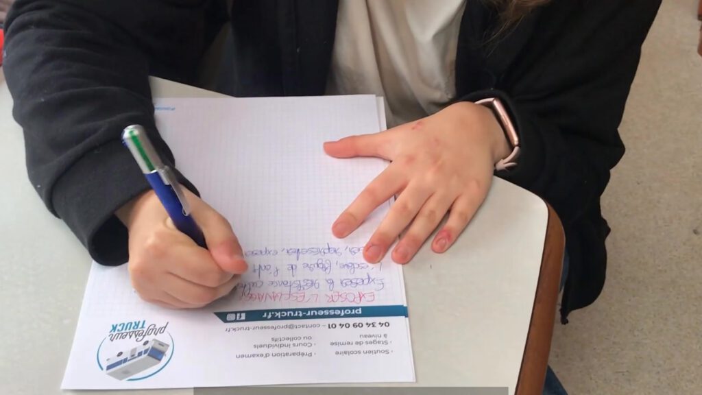 Une main écrit sur une fiche d’exercice posée sur la table du Professeur Truck.