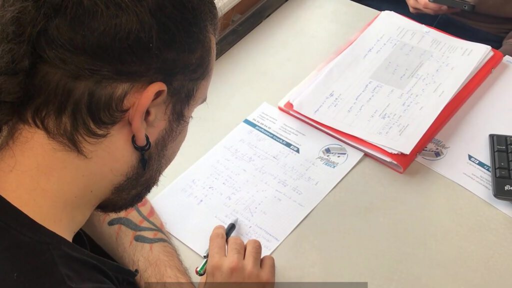 Vue du dessus de la table de travail, avec des exercices, un cahier et un clavier.